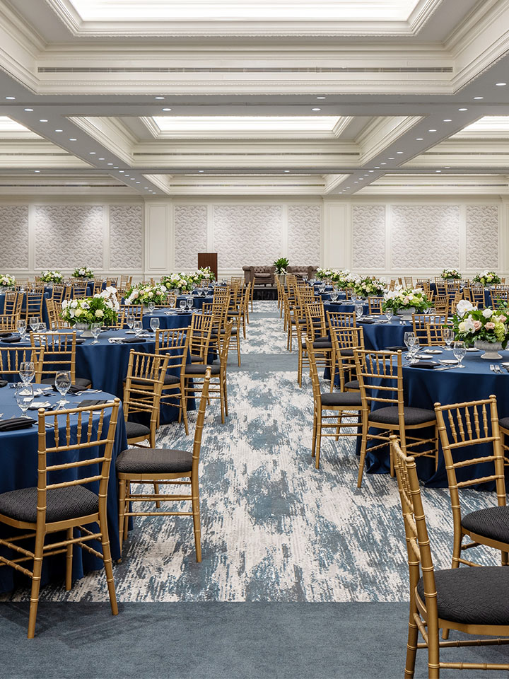 Ballroom with round tables dressed in blue tablecloths and wooden chairs