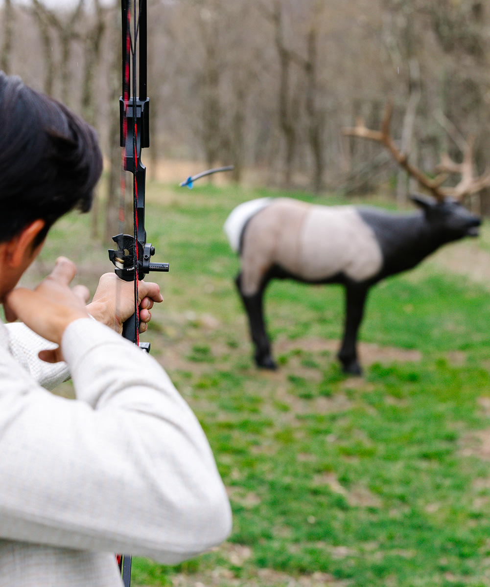 a person in a white show using a bow and arrow to aim at a 3D model of an elk