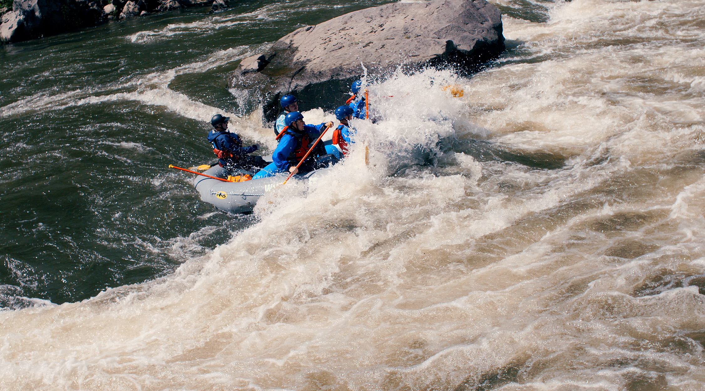 An inflatable raft with several people encountering white water on a river rafting experience