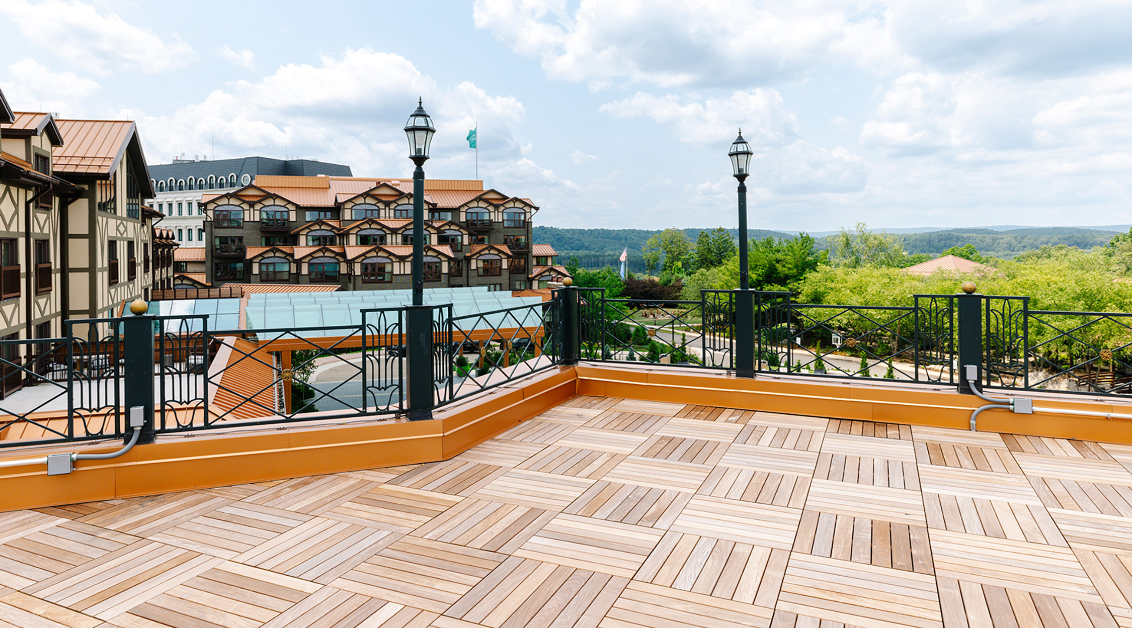 A rooftop deck of parquet wood overlooking a hotel, green mountains, and blue sky, on the Plaza Deck located at Nemacolin resort